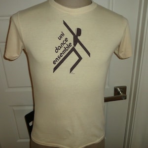May include: A beige t-shirt with a brown graphic of a stylized dancer and the text "uni dance ensemble".