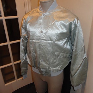 May include: A silver satin bomber jacket with a zip fastening and a pocket on the left side.