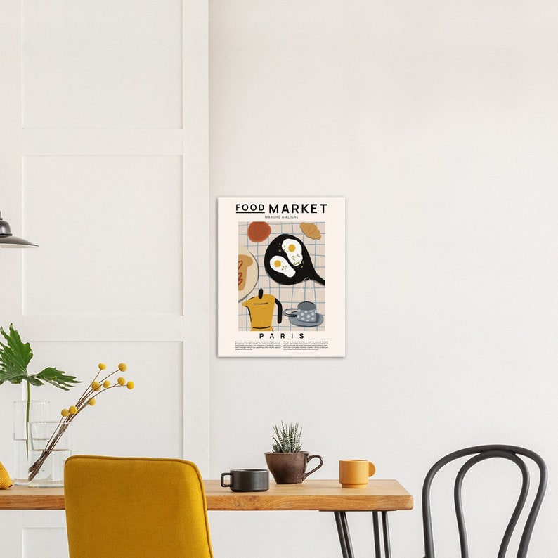 May include: A minimalist poster with a graphic illustration of a breakfast scene. The poster features a frying pan with two eggs, a coffee pot, a croissant, and a cup of coffee. The text "FOOD MARKET" and "PARIS" is printed on the poster.