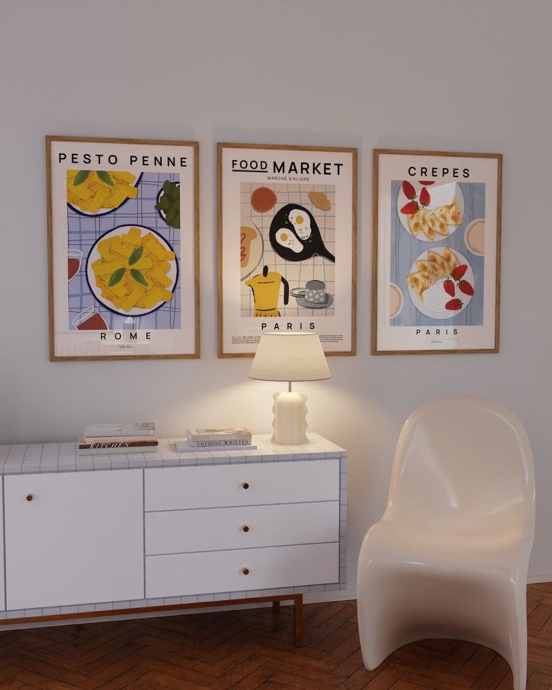 May include: Three framed illustrations of food with the titles "Pesto Penne Rome", "Food Market Paris", and "Crepes Paris". The illustrations are in a minimalist style with a blue and white checkered background.
