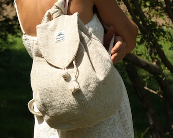 May include: A beige hemp backpack with a drawstring closure and a small label that says "Hemptique" on it. The backpack is being worn by a person in a white dress.