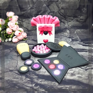 Könnte beinhalten: Ein rosa-weißer Kuchen, der mit einem Make-up-Thema verziert ist. Der Kuchen zeigt eine rosa-weiße Schachtel mit Schleife, eine rosa Rouge-Dose, eine schwarze Lidschattenpalette und einen Make-up-Pinsel.