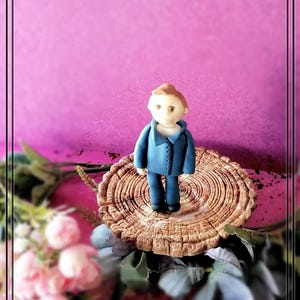 Könnte beinhalten: Eine kleine blaue Figur eines Menschen, der auf einem braunen Baumstumpf mit Ringen steht. Die Figur hat braunes Haar und ein weißes Hemd.