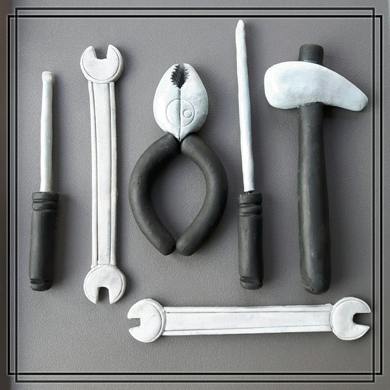 May include: A set of seven tools made of white and black clay, including a hammer, pliers, a screwdriver, a wrench, and a small knife. The tools are arranged on a gray background.