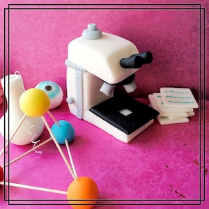 Könnte beinhalten: Ein weißes Fondant-Mikroskop mit schwarzen Details, ein blaues und gelbes Atommodell und ein weißes Fondant-Auge auf rosa Hintergrund.