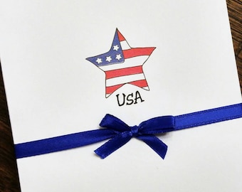 May include: A white card with a blue ribbon tied in a bow. The card has a red, white, and blue star with the word "USA" printed below it.