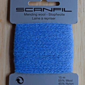 May include: A card of light blue mending wool by Scanfil. The packaging features the text Scanfil, Mending wool, Stopfwolle, Laine &agrave; repriser, 15 m, 55% Wool, and 45% Nylon. The blue yarn is wrapped horizontally around the centre of the grey card.