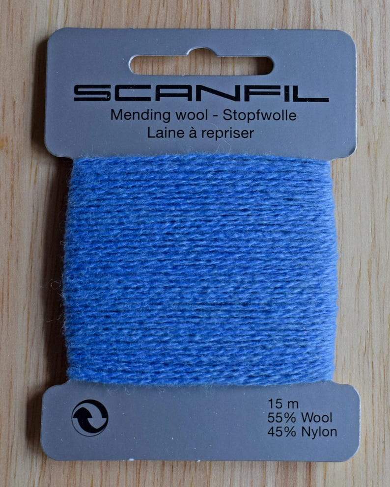 May include: A card of light blue mending wool by Scanfil. The packaging features the text Scanfil, Mending wool, Stopfwolle, Laine &agrave; repriser, 15 m, 55% Wool, and 45% Nylon. The blue yarn is wrapped horizontally around the centre of the grey card.