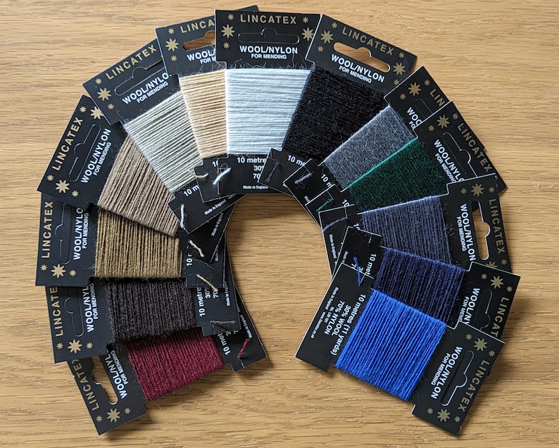 May include: A variety of 10-meter spools of wool/nylon thread for mending, in colors including beige, brown, black, red, blue, green, and gray. The spools are arranged in a semi-circle on a wooden surface. Each spool has a black label with the text "LINCATEX WOOL/NYLON FOR MENDING" and the length of the thread in meters.