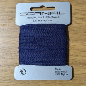 May include: A card of navy blue Scanfil mending wool wrapped around a light grey cardboard holder. The text reads Scanfil, Mending wool, Stopfwolle, Laine &agrave; repriser, 15 m, 55% Wool, and 45% Nylon. The yarn has a textured, matte finish.