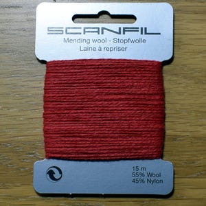 May include: A card of red mending wool by Scanfil. The light grey cardboard holder features the brand name, the text Mending wool - Stopfwolle Laine &agrave; repriser, and technical details stating 15 m, 55% Wool, and 45% Nylon with a recycling symbol.
