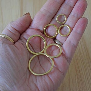May include: Five gold-coloured metal rings of different sizes, arranged in a circle on a person's palm.