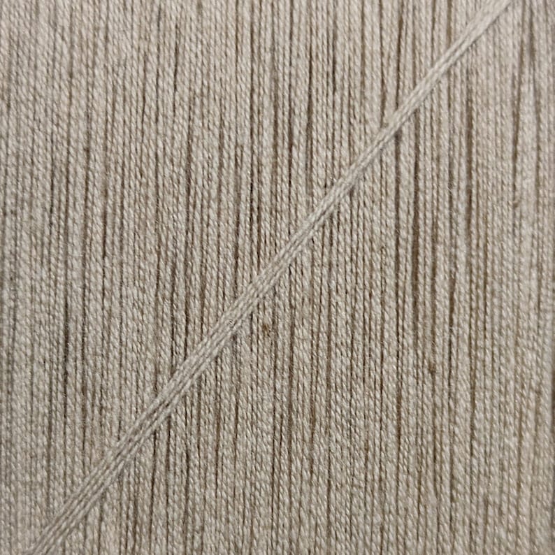 May include: Close-up of a beige woven fabric with a single, diagonal, lighter beige thread running across the surface.