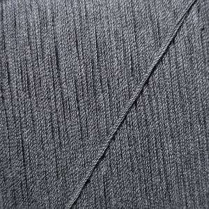 May include: Close-up of a dark gray fabric with a diagonal seam. The fabric has a textured, woven appearance.