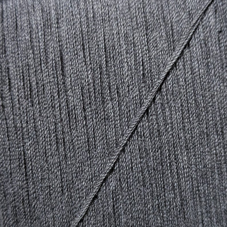 May include: Close-up of a dark gray fabric with a diagonal seam. The fabric has a textured, woven appearance.