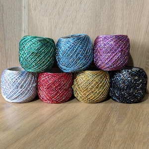 May include: Eight spools of sparkly yarn in various colours, including green, blue, purple, white, red, gold, black, and silver. The yarn is wound around cardboard spools.