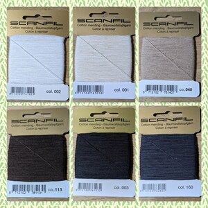 May include: Six spools of cotton mending thread in various colors, including white, beige, brown, black, and gray. Each spool is labeled with the brand name "SCANFIL" and the color number.