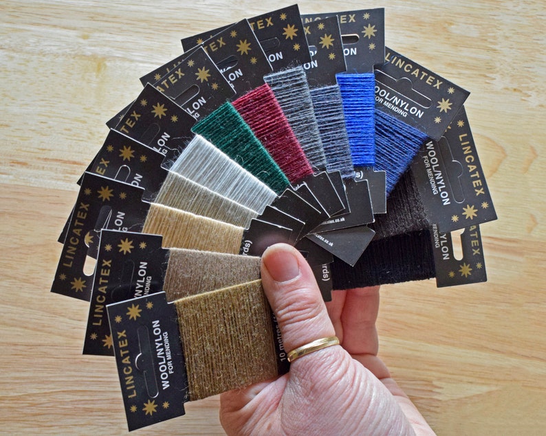 May include: A fan of 10 spools of wool/nylon thread for mending, in various colors, including black, blue, gray, red, green, beige, and brown. Each spool is labeled "Lincatex Wool/Nylon for Mending".