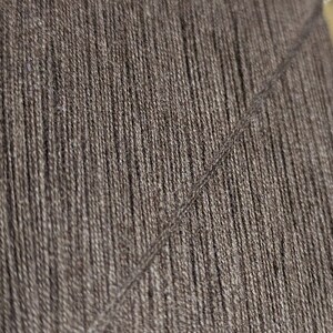 May include: Close-up of a dark brown yarn with a subtle sheen. The yarn is tightly woven and has a smooth texture.