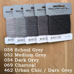 May include: Five Scanfil mending wool cards in a gradient of grey shades, ranging from light grey to dark charcoal. Each card features the brand name, product type, a barcode, and specific colour codes: 058 School Grey, 052 Medium Grey, 054 Dark Grey, 069 Charcoal, and 462 Urban Chic.