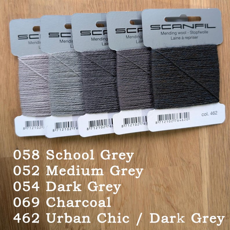 May include: Five Scanfil mending wool cards in a gradient of grey shades, ranging from light grey to dark charcoal. Each card features the brand name, product type, a barcode, and specific colour codes: 058 School Grey, 052 Medium Grey, 054 Dark Grey, 069 Charcoal, and 462 Urban Chic.