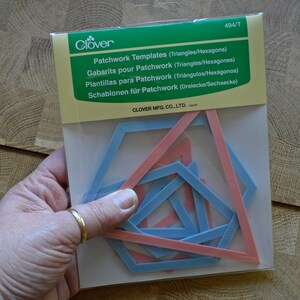May include: Clover brand patchwork templates for triangles and hexagons in a clear plastic package. The set includes multiple blue and pink geometric plastic frames of varying sizes for quilting and sewing projects, labelled with model number 494/T.