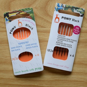 May include: Two packs of black tapestry needles. The pack on the left contains six needles sized 24/26. The pack on the right contains six needles sized 18/24. Both packs have the text "PONY Black" and "not nickel plated".