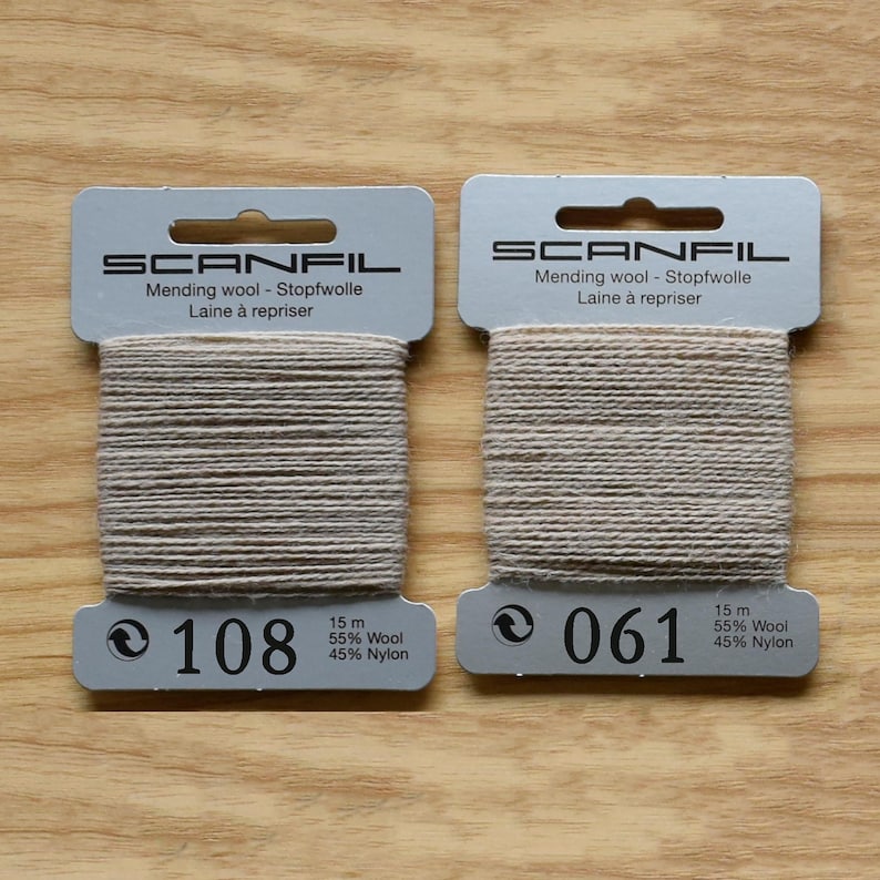 May include: Two rectangular cards of Scanfil mending wool in a light beige colour. Each card contains 15 metres of thread composed of 55% wool and 45% nylon. The cards are labelled with the numbers 108 and 061, indicating the specific colour shades.