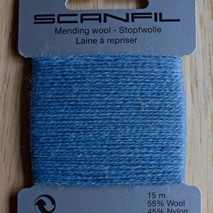 May include: A card of blue mending wool by Scanfil. The grey cardboard packaging features the brand name, the text Mending wool - Stopfwolle Laine &agrave; repriser, and the specifications 15 m, 55% Wool, and 45% Nylon printed in black ink.