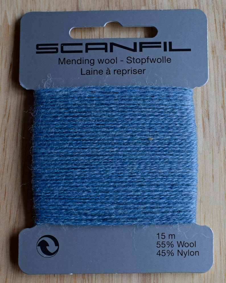 May include: A card of blue mending wool by Scanfil. The grey cardboard packaging features the brand name, the text Mending wool - Stopfwolle Laine &agrave; repriser, and the specifications 15 m, 55% Wool, and 45% Nylon printed in black ink.