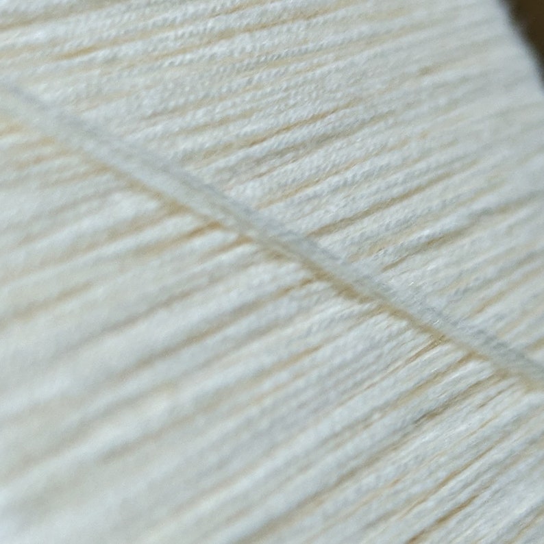 May include: Close-up of a white yarn skein, showing the individual strands of yarn.