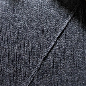 May include: Close-up of a black fabric with a diagonal seam. The fabric has a textured, woven appearance.