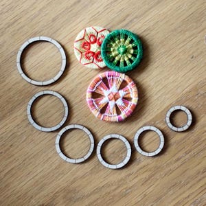 May include: A collection of wooden embroidery hoops and embroidered circular designs in various colours. The stitched circles feature red, green, and orange thread patterns. The wooden hoops are various sizes.