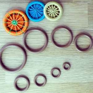 May include: A set of eight brown rubber rings of varying sizes, arranged in a semi-circle shape. Three colourful fabric buttons with a starburst design are placed above the rings.