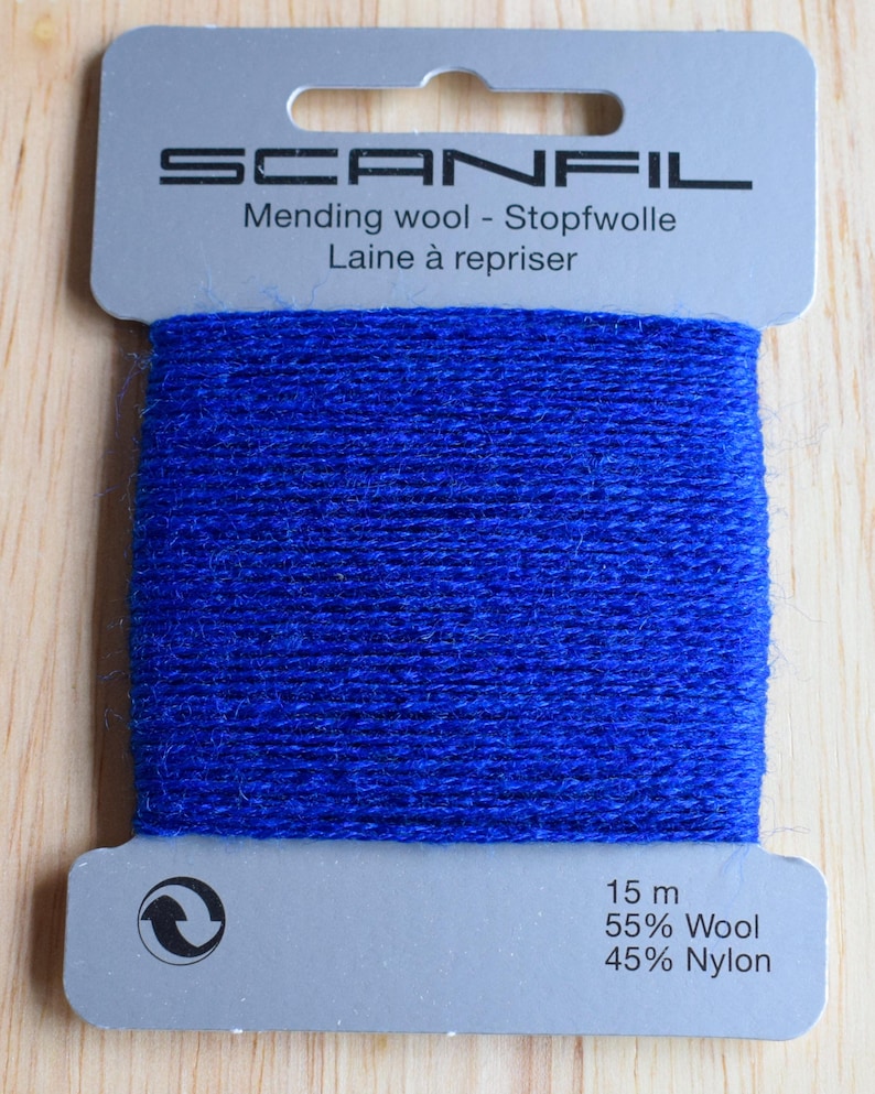 May include: A card of bright blue mending wool by Scanfil. The grey cardboard packaging features the brand name, the text Mending wool - Stopfwolle - Laine &agrave; repriser, and specifies 15 m of thread composed of 55% Wool and 45% Nylon.