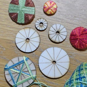 May include: Assortment of embroidery hoops with different coloured threads and designs. The hoops are made of wood and have a circular shape. Some of the hoops are finished with embroidery, while others are blank.