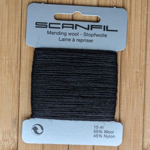 May include: A card of black mending wool by Scanfil. The grey cardboard packaging features the brand name, the text Mending wool - Stopfwolle - Laine &agrave; repriser, and specifies 15 m of thread composed of 55% Wool and 45% Nylon with a circular icon.
