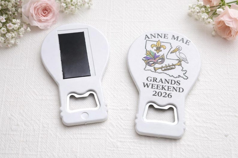 May include: Two white bottle openers with a magnetic back. One shows a graphic of the state of Louisiana, a fleur-de-lis, a mask, a pelican, and a trumpet, with the text ANNE MAE GRANDS WEEKEND 2026. The other shows the plain white back with a magnet.