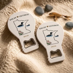 May include: Two white bottle openers featuring a black outline of the state of Minnesota, a loon, a small boat, and pink flowers. The text reads SALAS GETAWAY and 2026. The design includes a heart symbol between the words SALAS and GETAWAY.