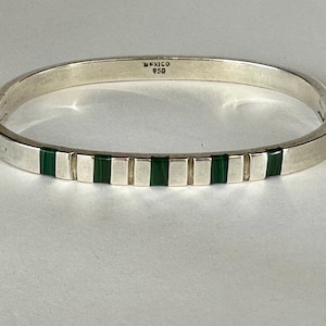 May include: A silver hinged bangle bracelet with rectangular green malachite inlays. The bracelet is marked "MEXICO 950". The bracelet is a piece of jewelry.
