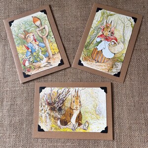 Peut inclure: Trois cartes de vœux avec des illustrations de lapins dans un jardin. Les cartes ont des bordures marron et des coins noirs. Les illustrations représentent des scènes avec des lapins, un oiseau et des outils de jardin.