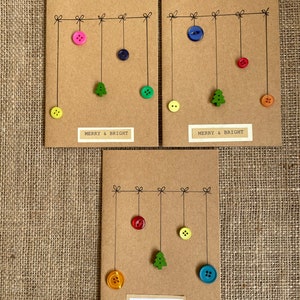 Könnte beinhalten: Drei handgefertigte Weihnachtskarten aus braunem Karton. Jede Karte zeigt bunte Knöpfe und einen kleinen grünen Baumschmuck, der an einer Linie hängt. Der Text "MERRY & BRIGHT" oder "merry christmas" ist auf den Karten aufgedruckt.