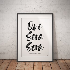 Op de afbeelding: Zwart-wit typografieprint met de woorden "Que Sera Sera" en de zin "Whatever will be will be".