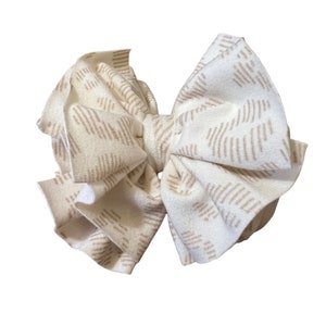 Peut inclure: Un grand nœud en tissu blanc avec un motif géométrique brun. Le nœud est fait d'un tissu doux et plissé et est parfait pour ajouter une touche de fantaisie à n'importe quelle tenue.