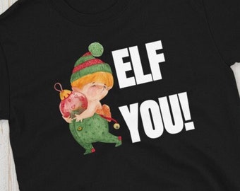 Peut inclure: T-shirt noir avec un graphique blanc d'un lutin tenant un ornement rouge. Le texte "ELF YOU!" est imprimé en blanc sur le t-shirt.