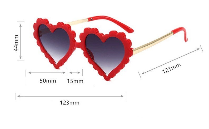 May include: Red heart-shaped sunglasses with gold arms and a scalloped edge. The sunglasses measure 123 mm wide, 44 mm tall, and 50 mm across the lenses.
