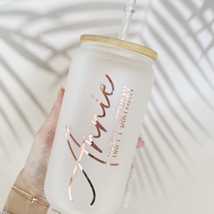 K&ouml;nnte beinhalten: Ein mattierter Glasbecher mit Bambusdeckel und einem klaren Strohhalm. Der Becher hat eine ros&eacute;farbene Aufschrift mit dem Text "Annie Happy Birthday" und den Text "BUBBLYZONE" am Boden.