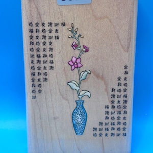 May include: A rectangular wooden rubber stamp featuring a central illustration of a purple orchid in a blue patterned vase. The stamp is decorated with columns of Chinese characters on both sides and includes the number 8374 on a label at the top.