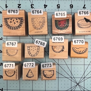 May include: A collection of wooden stamps featuring watermelon designs. The stamps vary in size and detail, with some showing a whole watermelon and others slices. Each stamp has a number label.