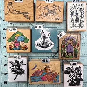 May include: A collection of wooden stamps featuring various whimsical designs. The stamps include mermaids, fairies, and other fantasy figures. The stamps are in various sizes and shapes, with detailed illustrations.